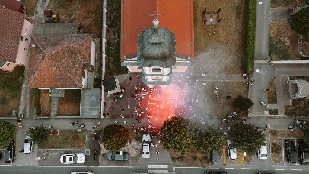 Leteći dron snima mladence kako izlaze iz crkve u danu, dok se baklje pale i stvaraju toplu i svečanu atmosferu na otvorenom.