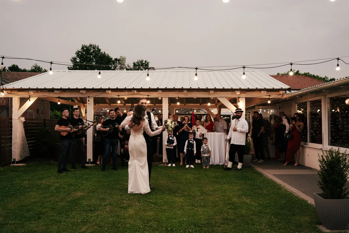 Ples mladenaca na tratini pod otvorenim nebom punoj uzvanika, okružena osmjesima i svečanom atmosferom.