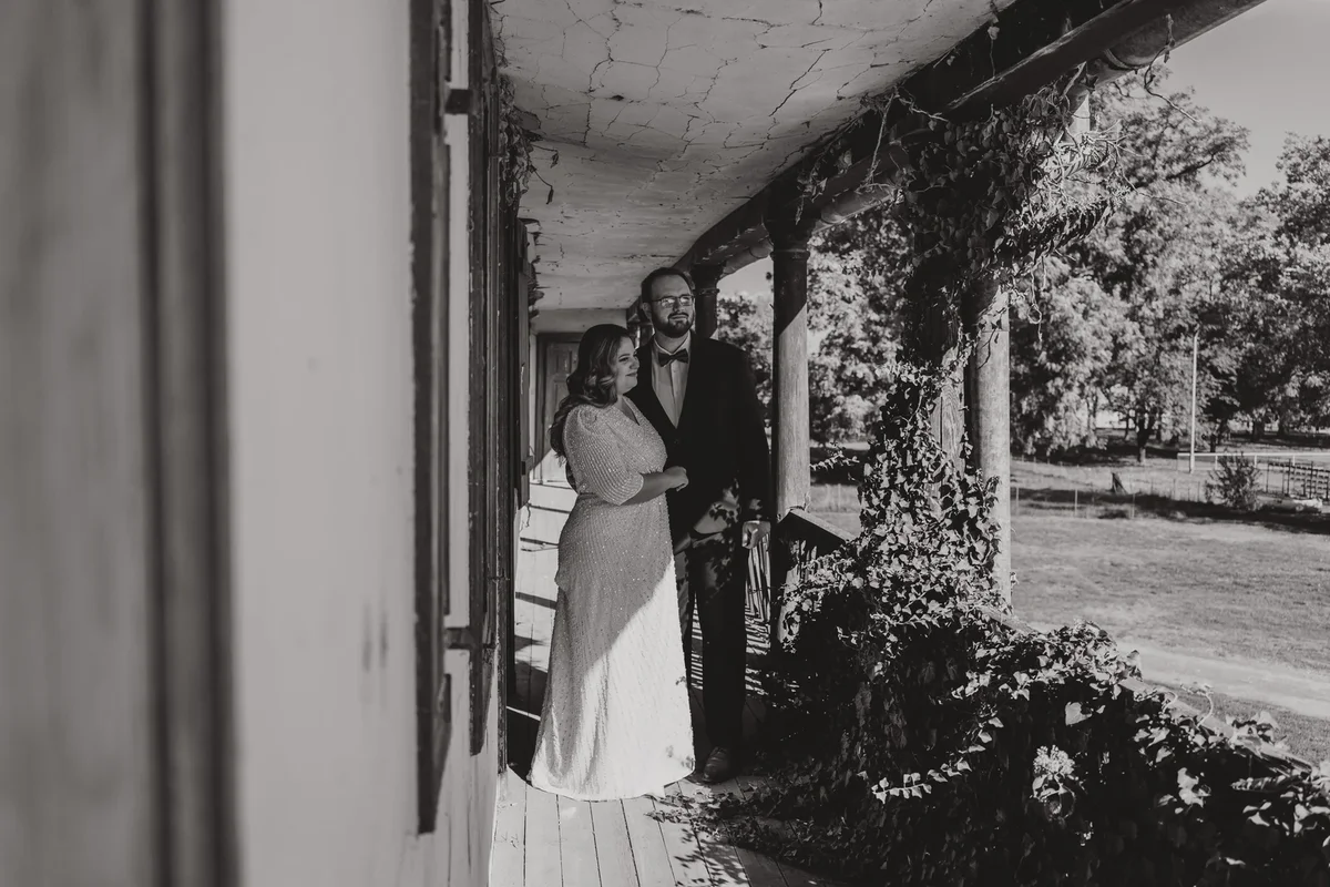 Crno-bijela fotografija mladenca i mladenke na trijemu stare kuće u slavonskom okruženju.